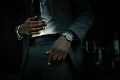 身穿黑色西装夹克和黑色裤子的男子，戴着银色圆形模拟手表